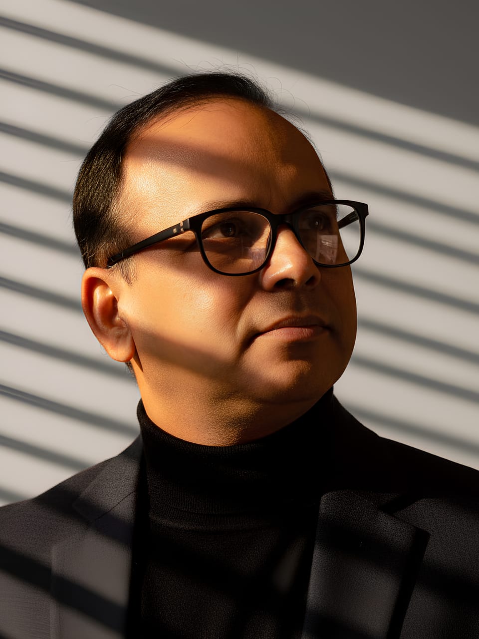 Dr. Mashiur Rahman — biotechnology and digital-health innovator, in a dark turtleneck lit by sunlight through window blinds